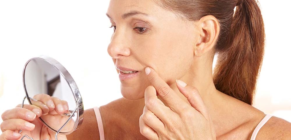 woman looking at smile lines in small mirror