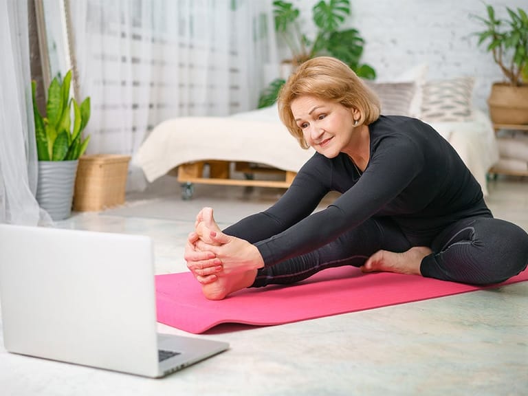 older woman stretching on yoga mat before exercise