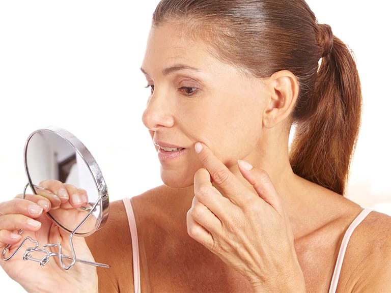 woman looking at smile lines in small mirror